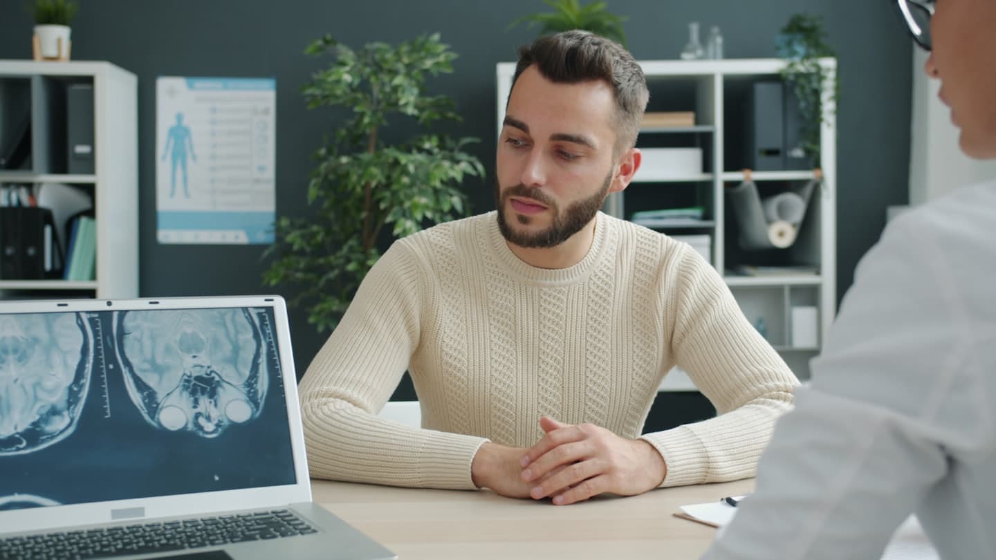 Lékař probírá výsledky vyšetření mozku s pacientem na notebooku.